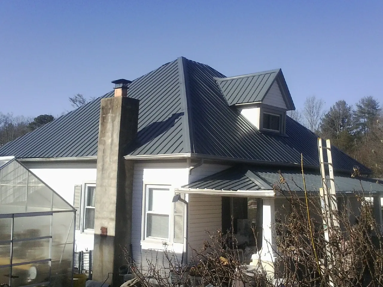 Dark blue standing seam metal roof on a white farmhouse with dormer — Slate & Tile Roof Repair by Roofing Brothers in Penn Yan