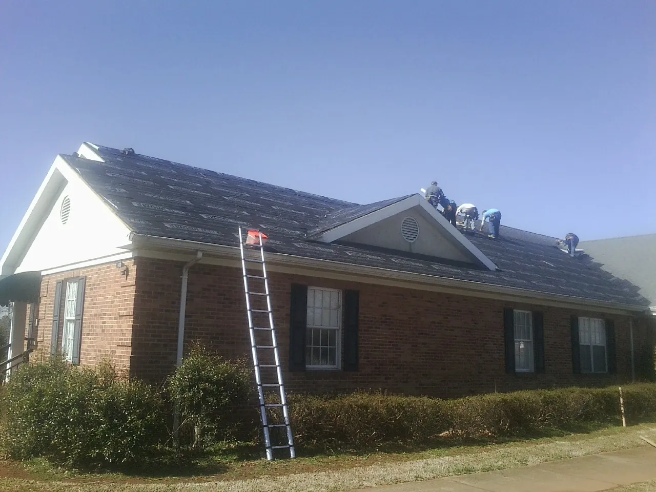 Crew tearing shingles off a brick ranch roof with a ladder set — Emergency Roof Repair work by our crew in Penn Yan