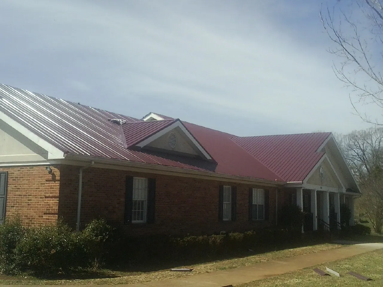 Red metal roof with gabled entries on a long brick building, from a Hail Damage Roof Repair job in Penn Yan