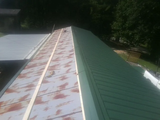 Old rusted panels beside newly installed green metal roofing — Wind Damage Roof Repair by Roofing Brothers in Penn Yan