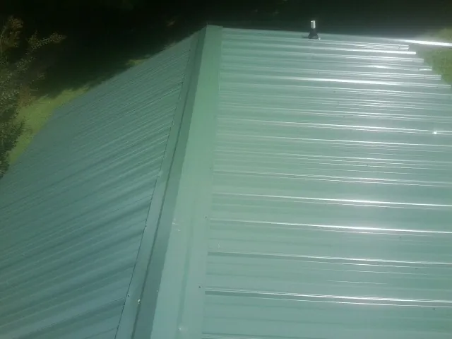 New green metal panels meeting at the ridge of a roof — Flat Roof Repair work by our crew in Penn Yan