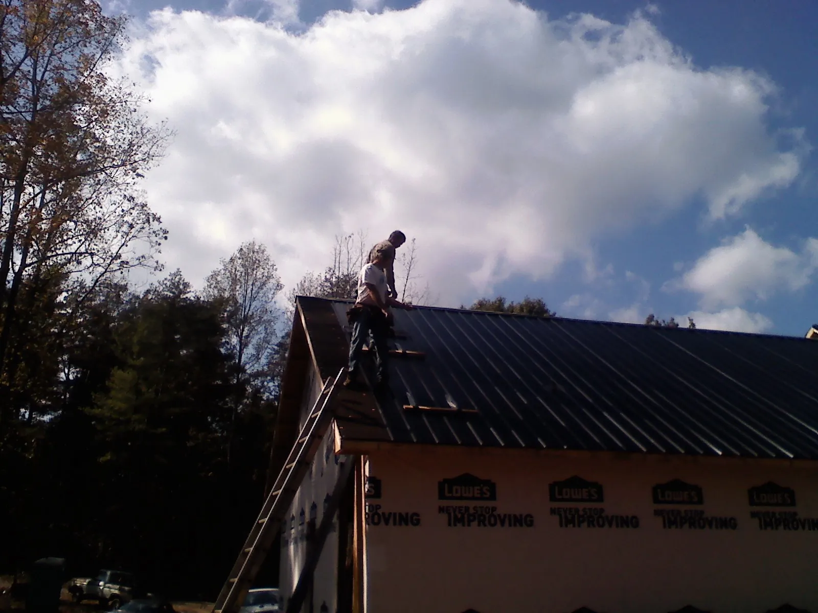 Roofer fastening dark metal panels high against a cloudy sky, from a Roof Inspection job in Penn Yan