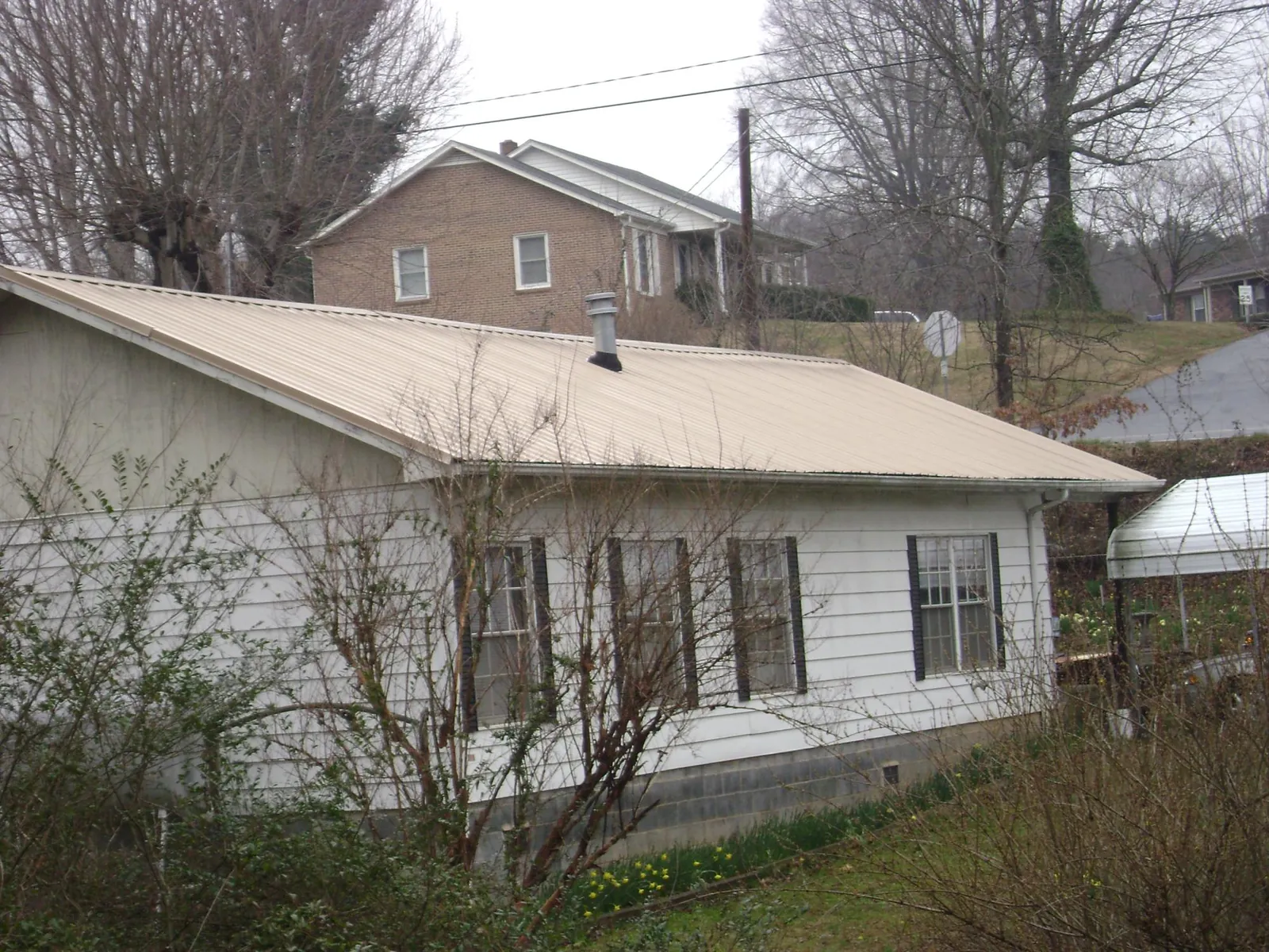 Tan metal roof on a white sided house set into a hillside — Commercial Roofing by Roofing Brothers in Penn Yan
