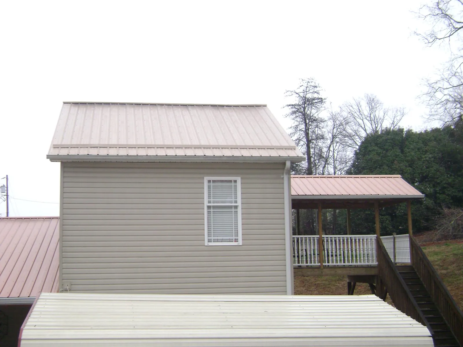 Tan metal roofs on a two story addition and attached porch, from a Roof Replacement job in Penn Yan